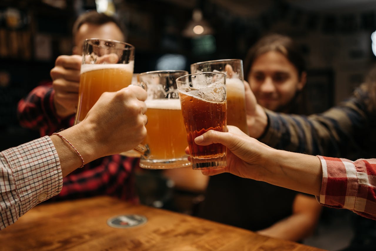 a beginner's guide to drinking beer with a group of men clinking their glasses