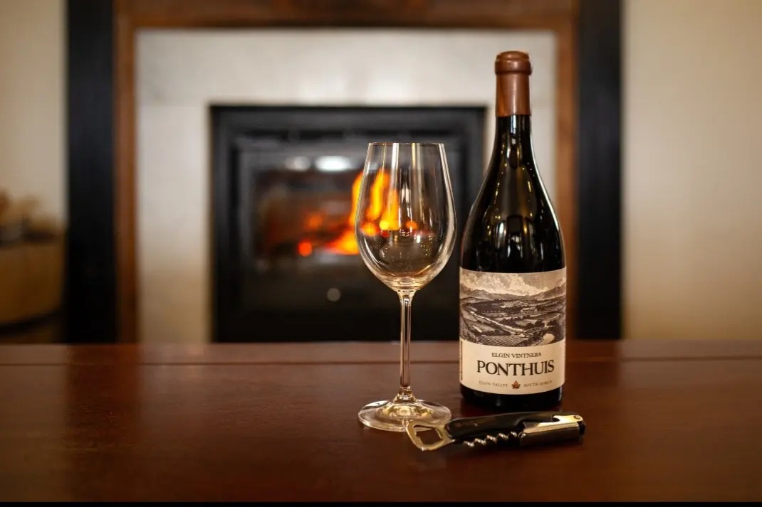 Exploring Elgin Valley Wine with bottle of elgin vintners ponthuis pinot noir and glass on table in front of fireplace