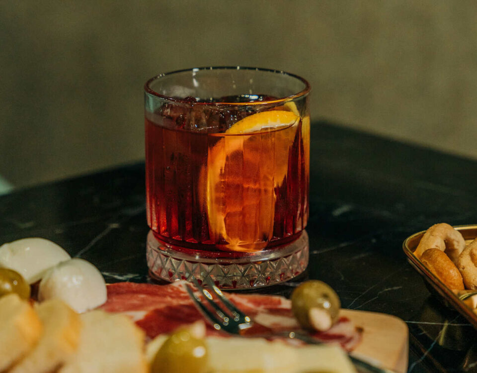 a botanical drink with an orange slice next to a snack board, illustrating one of the best non-alcoholic drinks