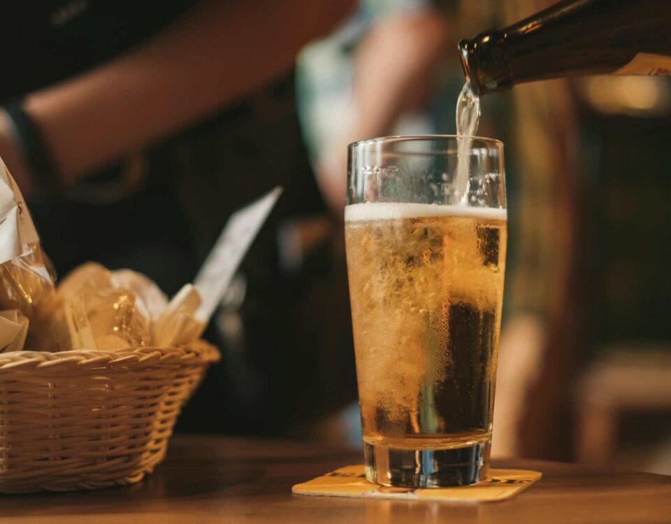 beer being poured inside glass from a bottle as part of illustrating the Draught Beer vs Bottled Beer debate
